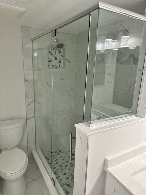 Modern bathroom with glass shower enclosure, white tiles, toilet, and vanity.
