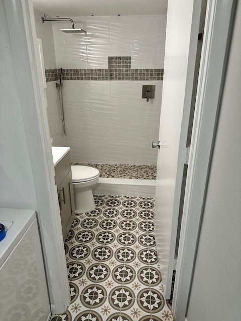 Bathroom with patterned floor tiles, white walls, and a shower with a pebble floor and decorative tile border.