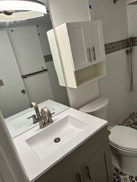 Bathroom with gray vanity, white sink, toilet, and a white cabinet above it. White and mosaic tiles.