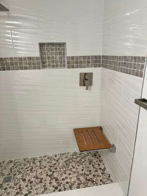 Accessible shower with white and mosaic tile, built-in wooden seat, and chrome fixtures.