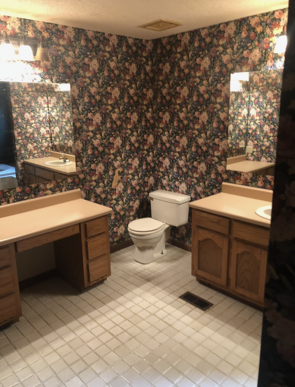 Bathroom with floral wallpaper, two vanities, toilet, mirrors, and white tiled floor.