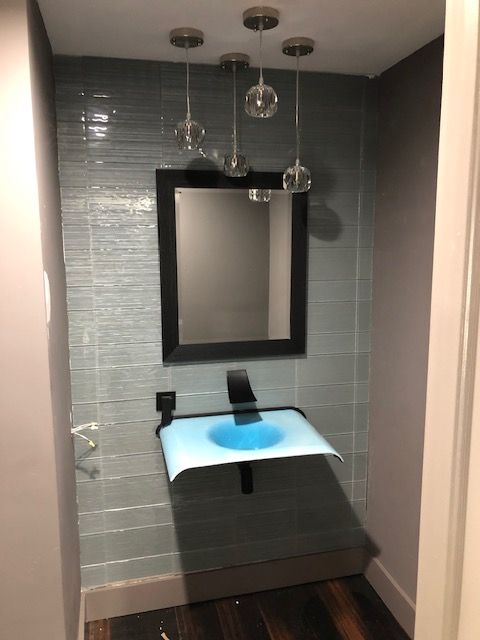 Small bathroom with blue tiled wall, black mirror, black sink, and pendant lights.