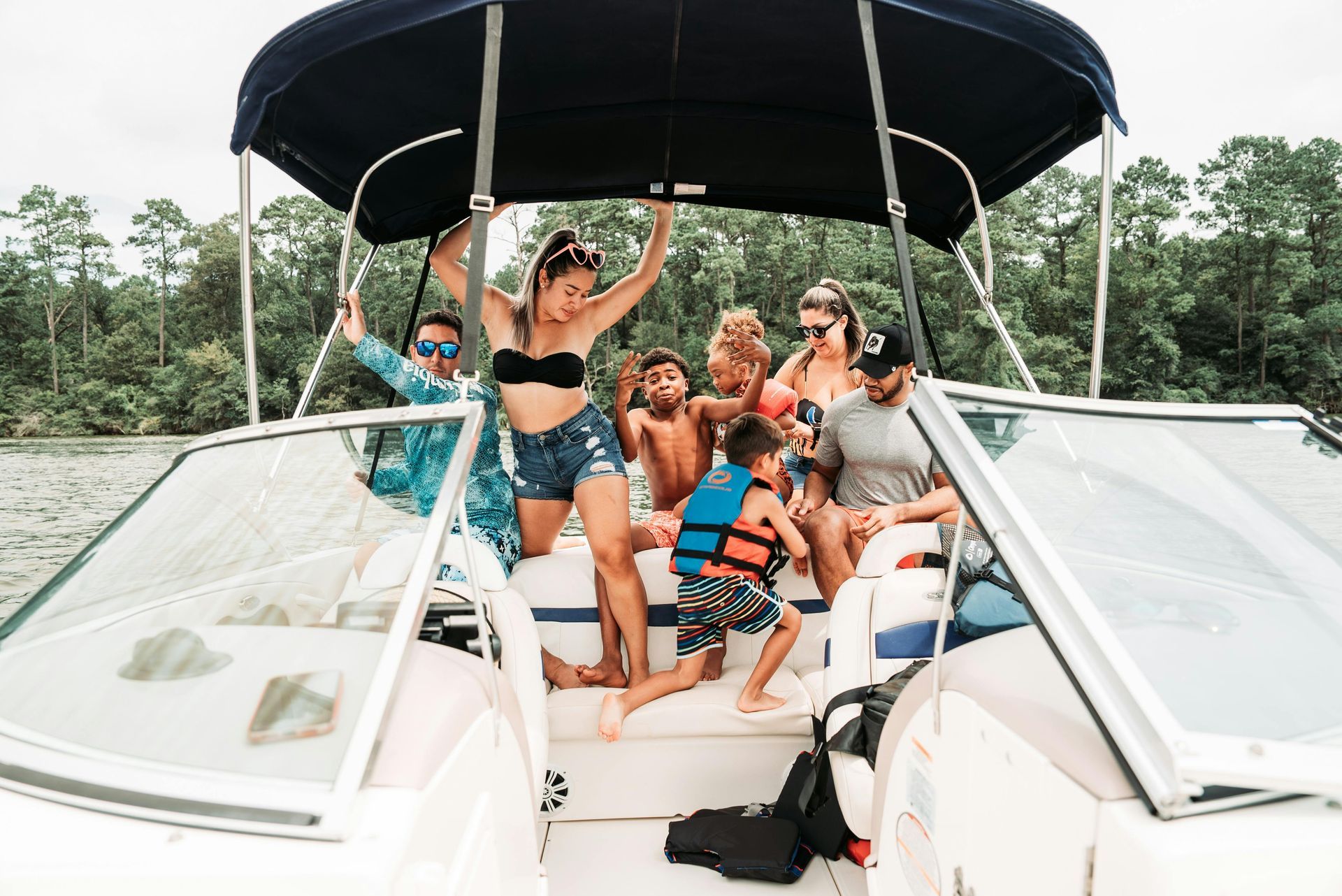 A group of people on a boat, some standing and waving, on a lake surrounded by trees.