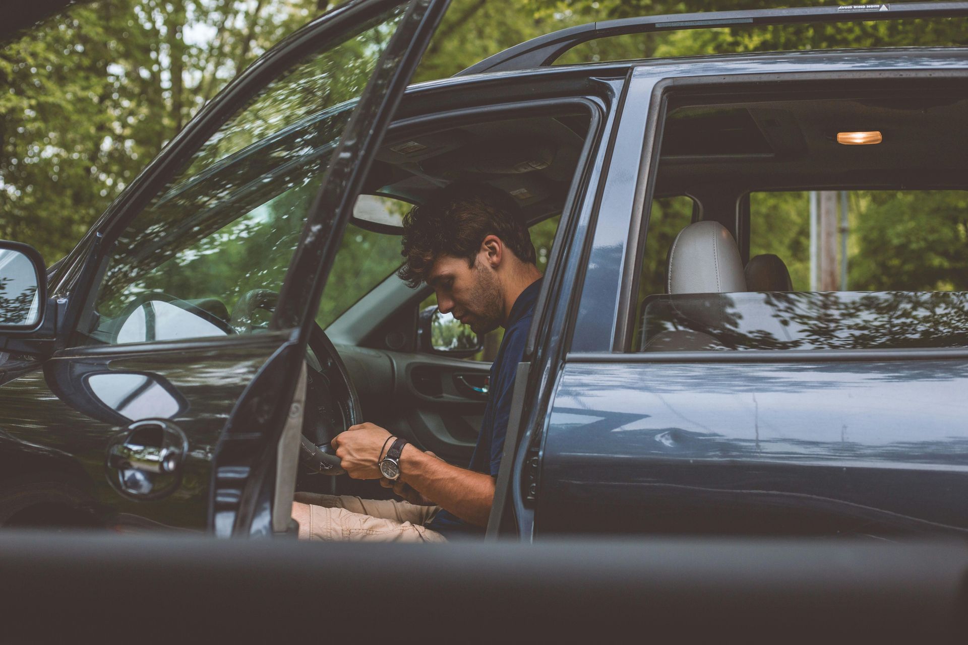 Three people smile while looking out the windows of a dark car on a sunny day.