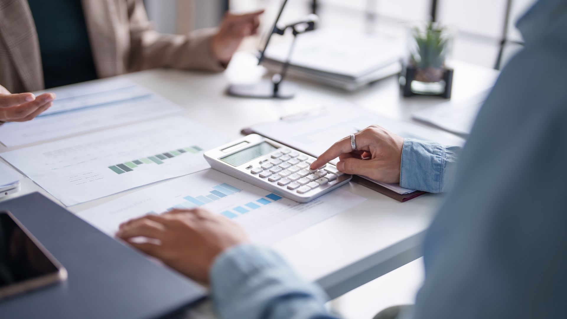 People reviewing financial documents and using a calculator at a white desk