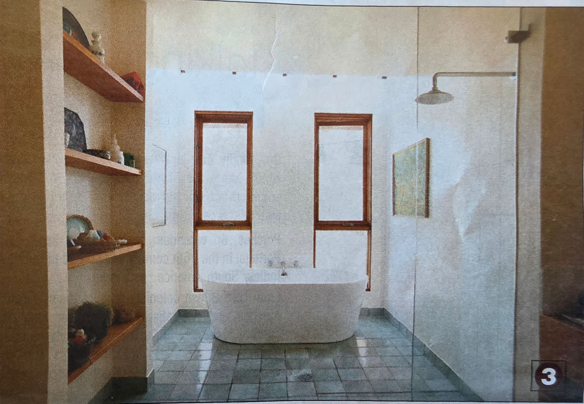 Bathroom with bathtub centered beneath two windows, tiled floor, showerhead, and built-in shelving.