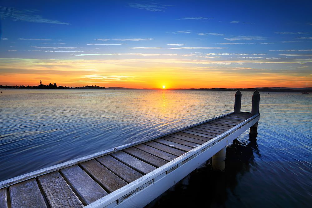 A Wooden Dock Overlooking A Body Of Water At Sunset — Lake Macquarie Podiatry in Belmont, NSW
