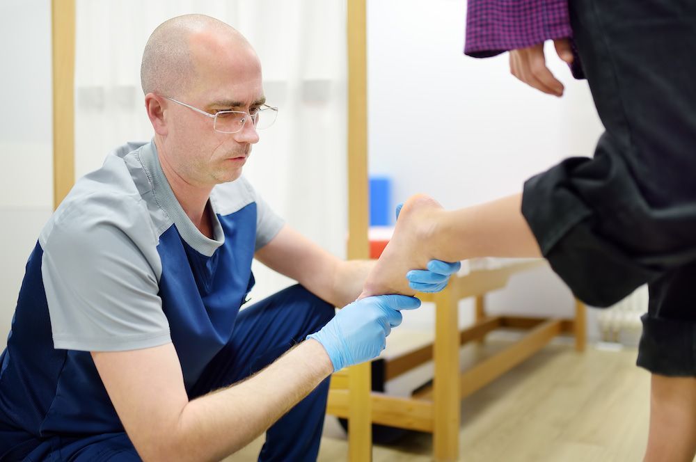A Doctor Is Examining A Patient's Foot With Blue Gloves — Lake Macquarie Podiatry in Belmont, NSW