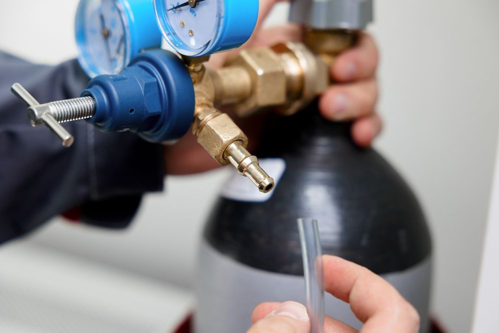 A person is holding a hose in front of a gas cylinder — Gastech Plumbing Services in Andergrove, QLD