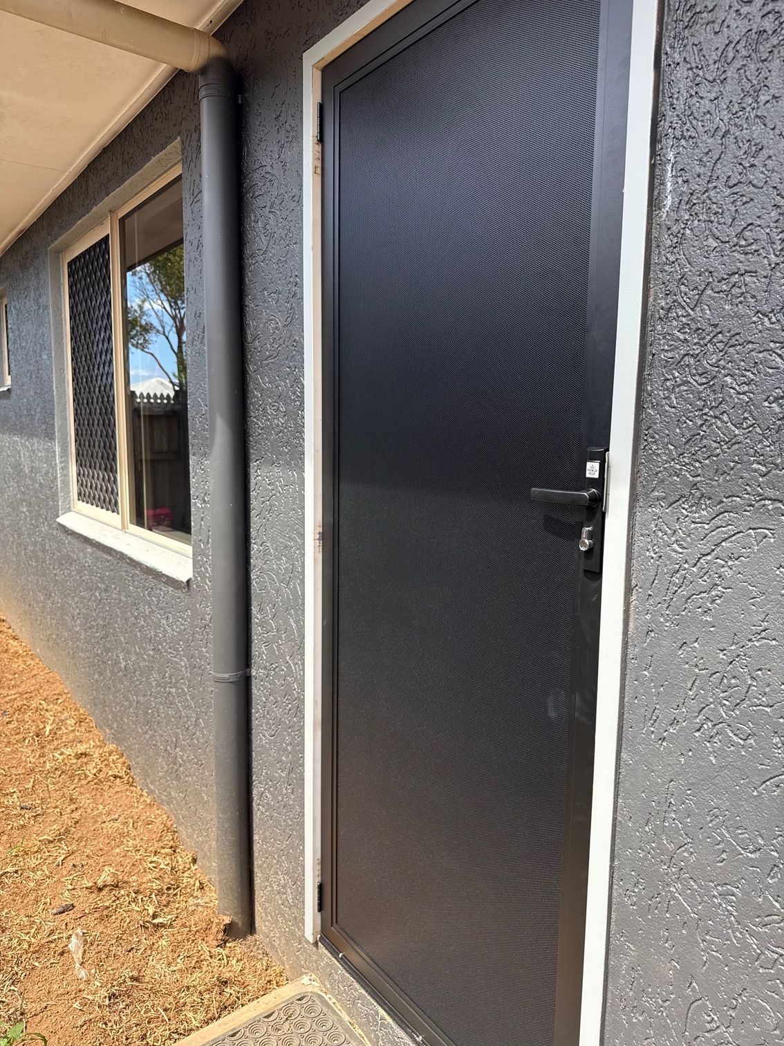 Black Security Door on a Gray Stucco Building — All Security Screens & Repairs In Bungalow, QLD