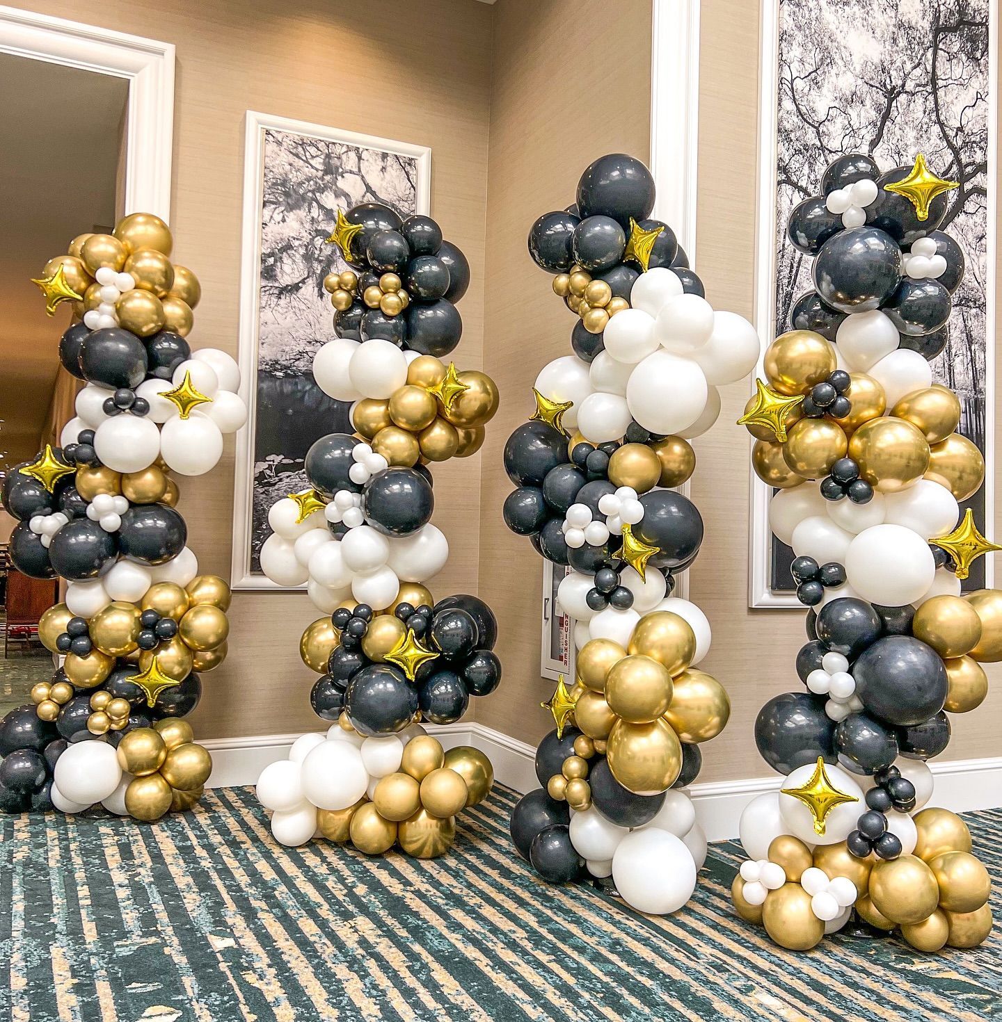 Four balloon columns in black, gold, and white, adorned with star accents, likely for a celebration.