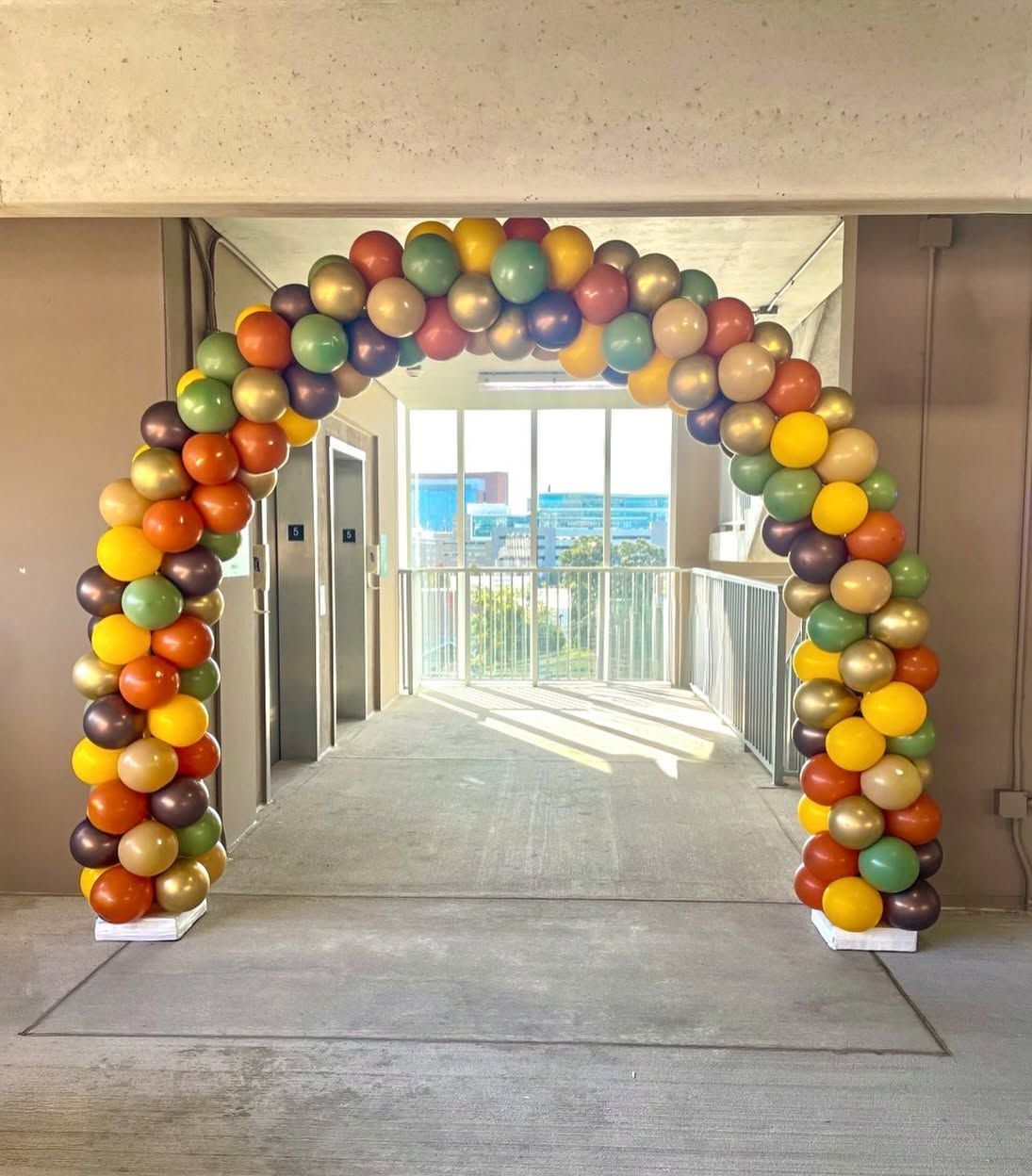 Colorful balloon arch in a hallway leading to a bright outdoor view