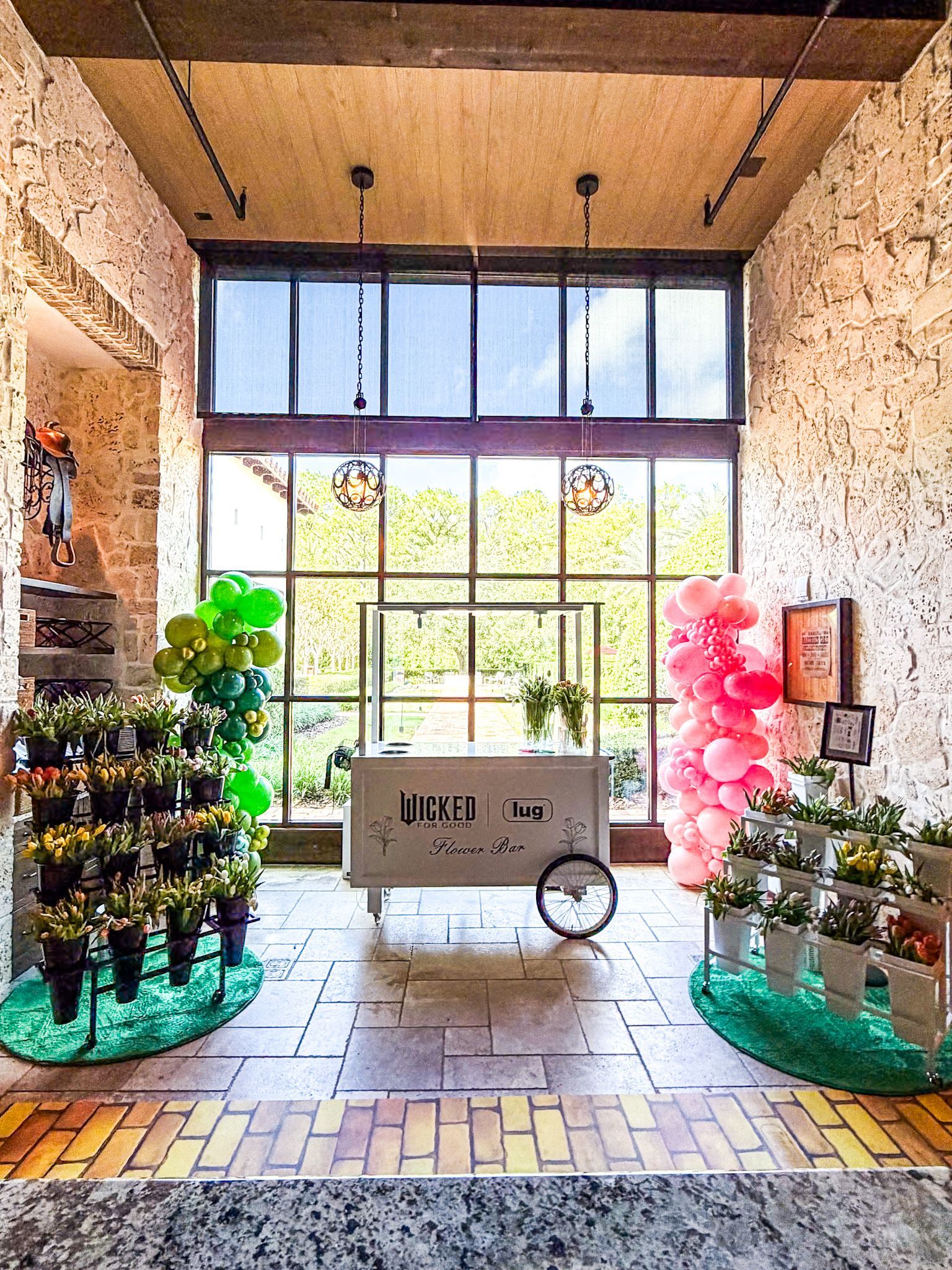 Flower shop interior with balloons, a cart, and potted plants in front of a window.