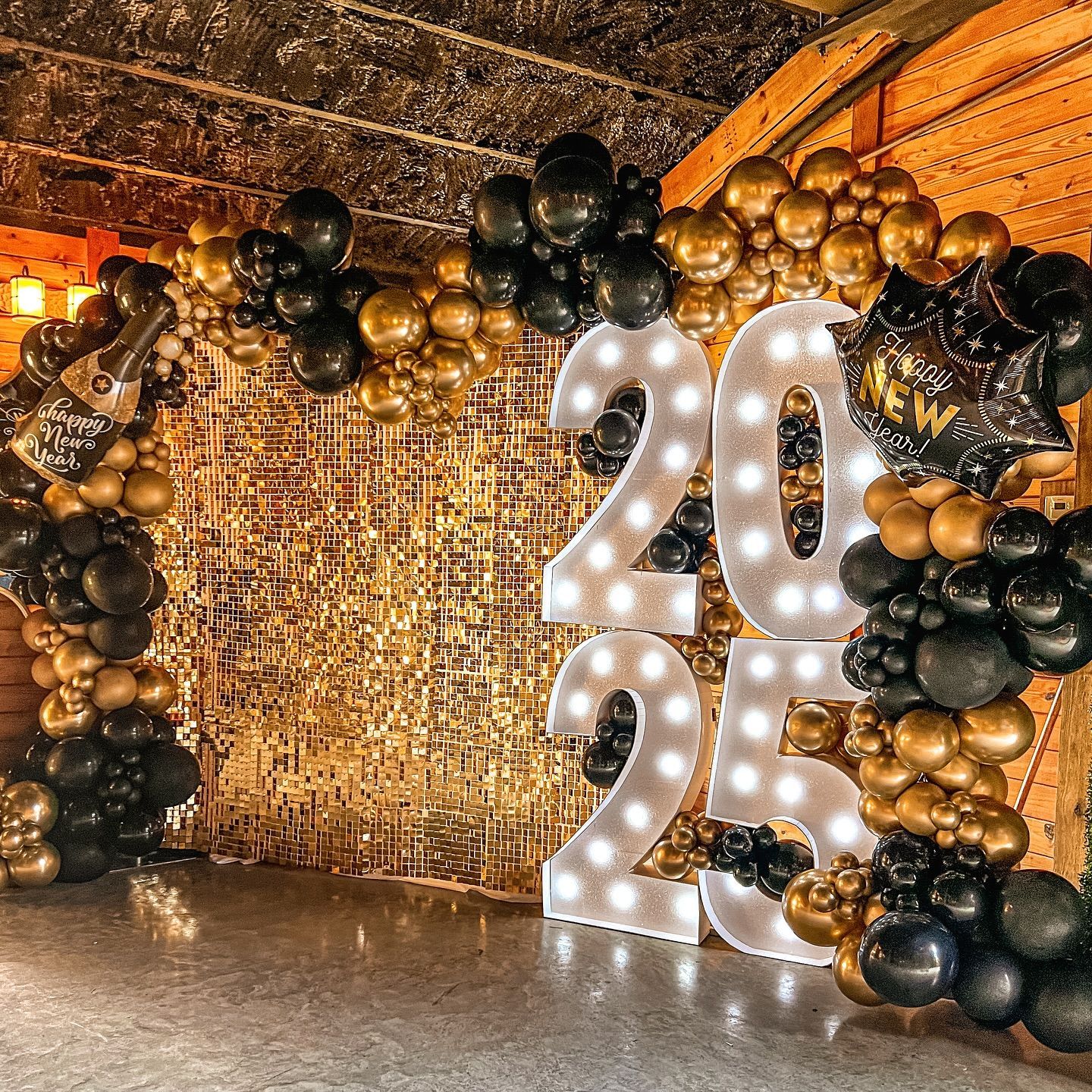 New Year's Eve party backdrop with a 2025 sign, gold and black balloons, and a golden backdrop.