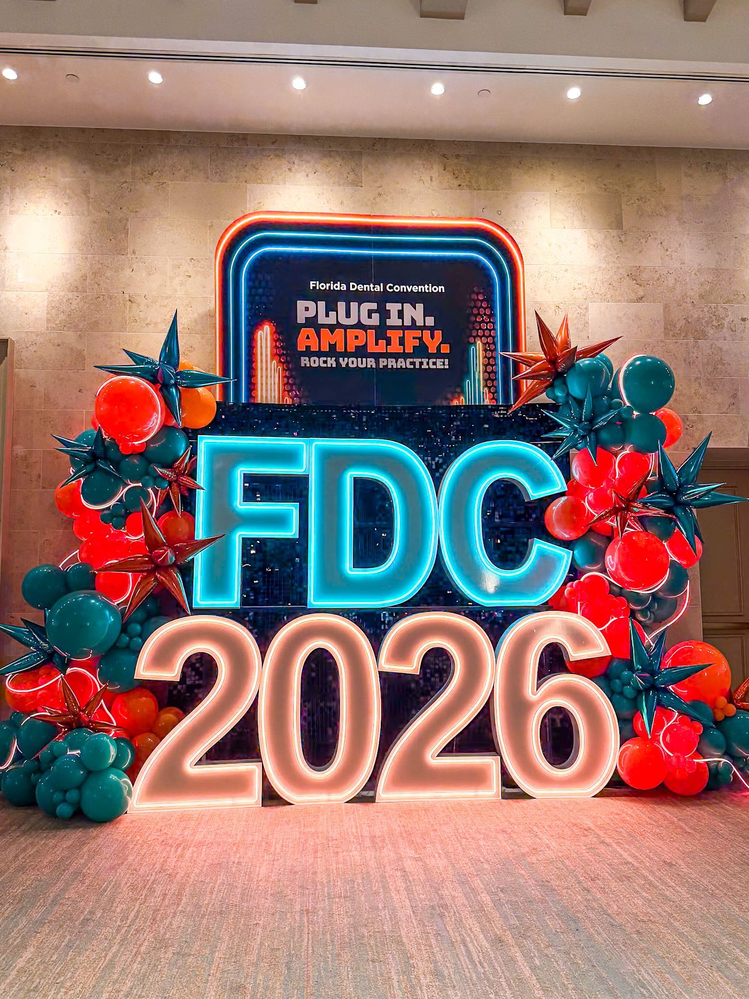 FDC 2026 neon sign with festive red and teal holiday decorations on a stage backdrop