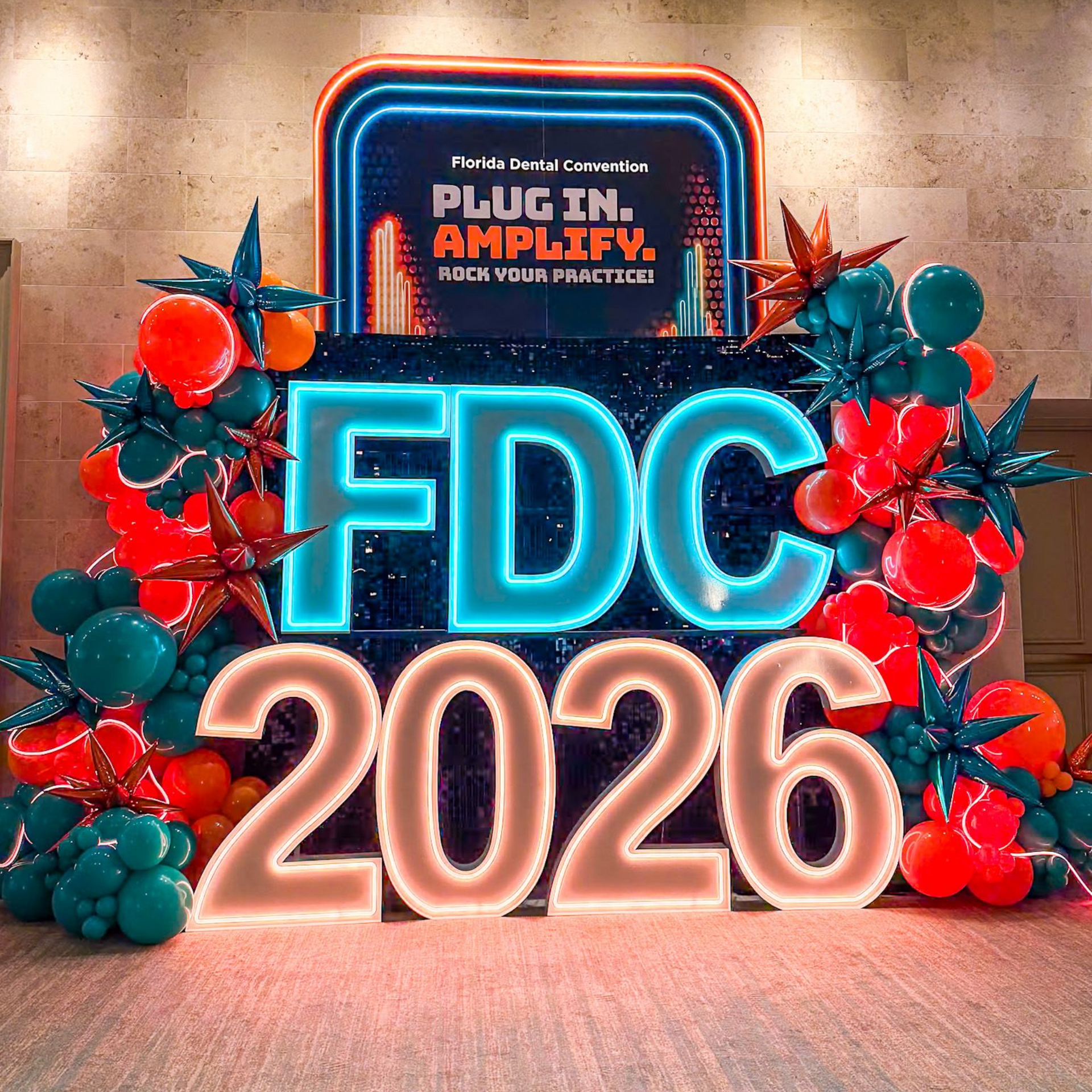 FDC 2026 neon sign with festive red and teal holiday decorations on a stage backdrop