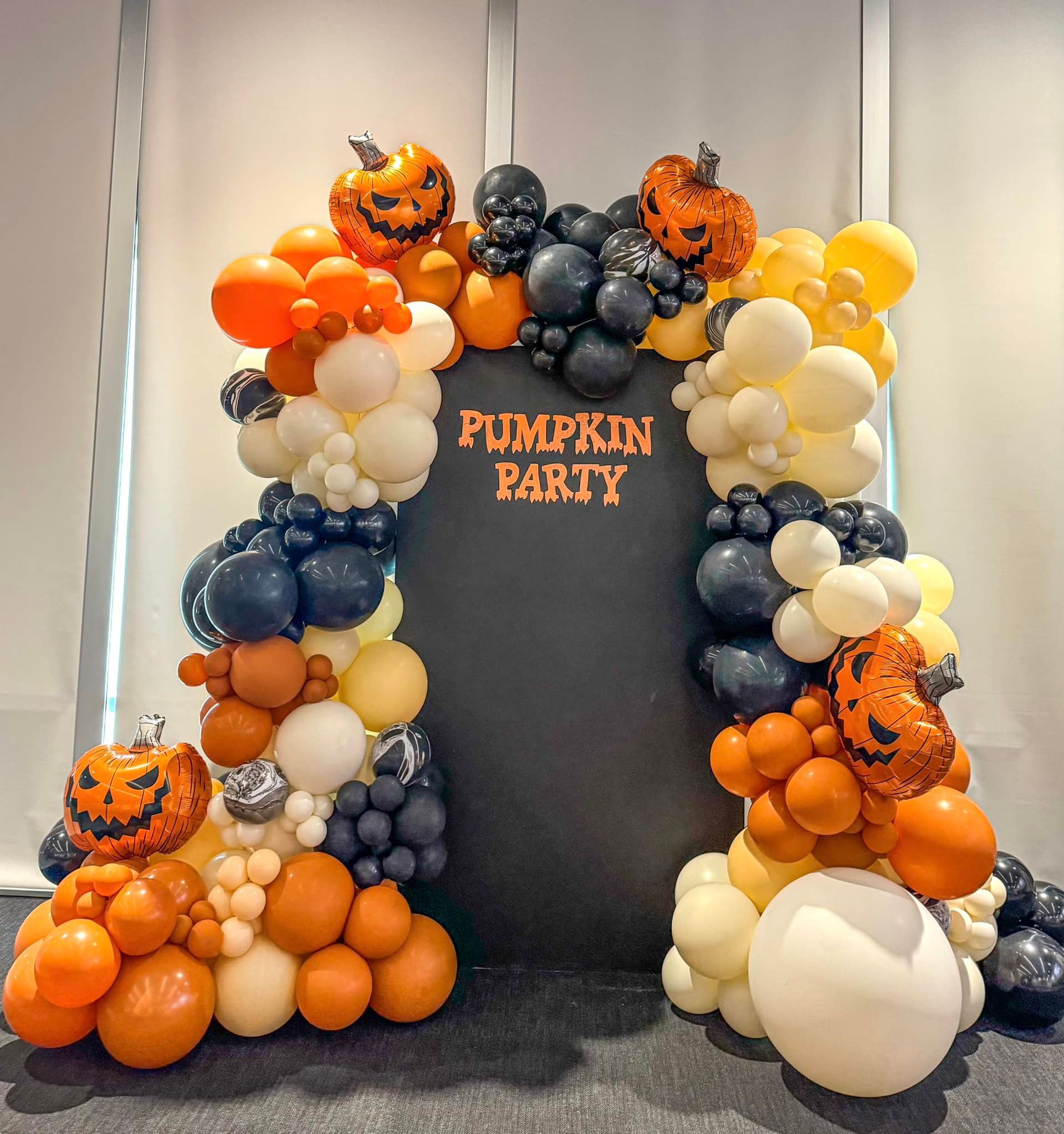 Pumpkin Party sign framed by orange, black, white, and yellow Halloween balloon garlands with jack-o’-lantern accents