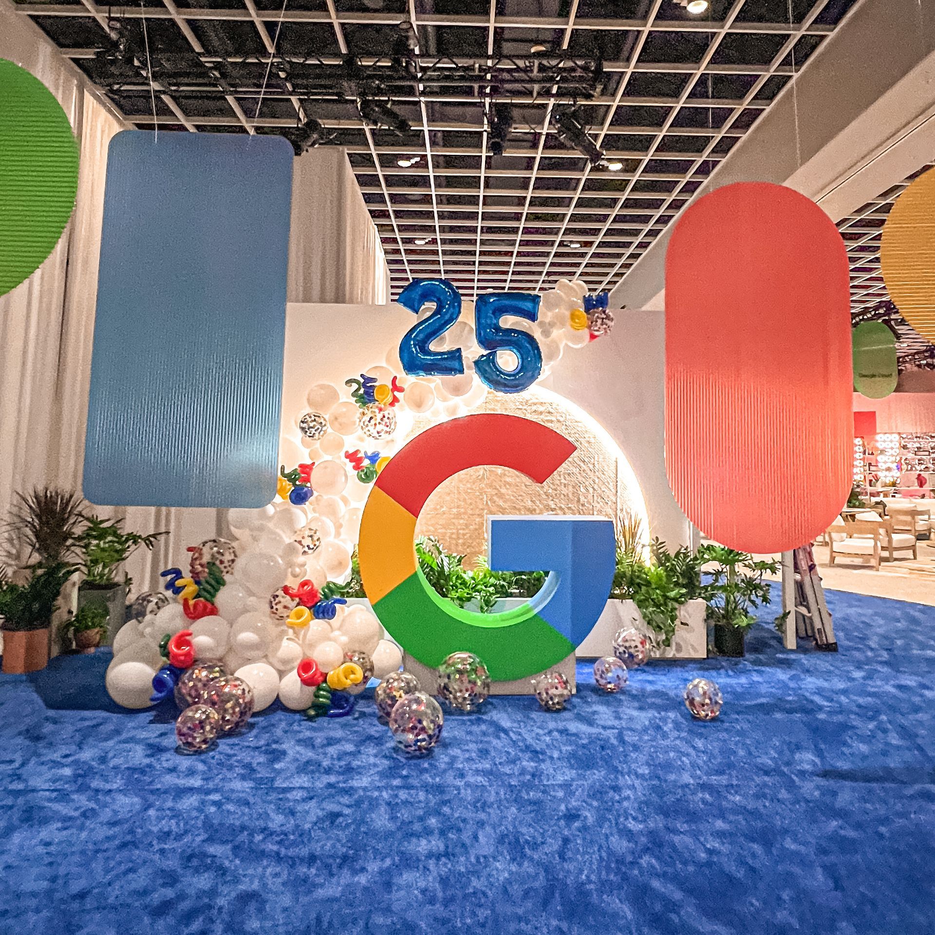 A large google sign is surrounded by balloons and plants