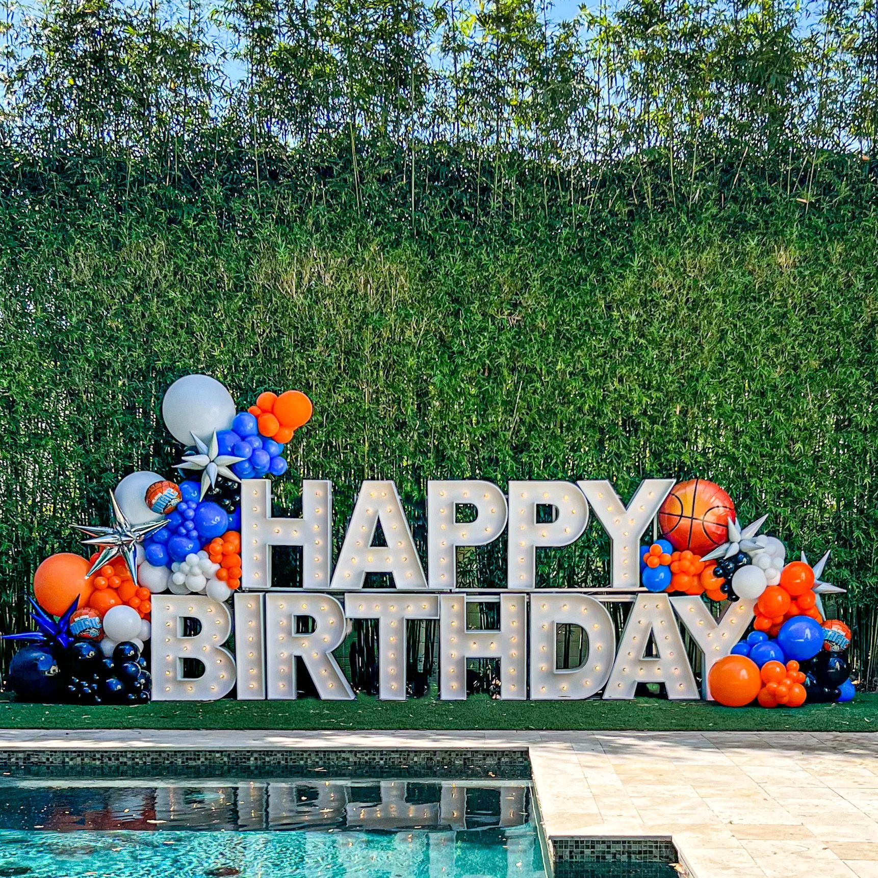 A large happy birthday sign with balloons in front of a pool.