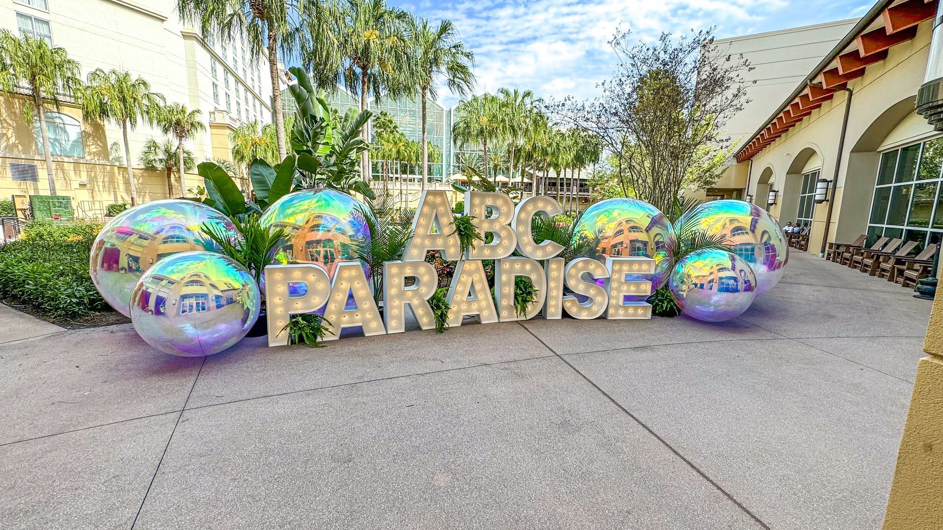 A sign that says abc paradise is surrounded by balloons on a sidewalk.