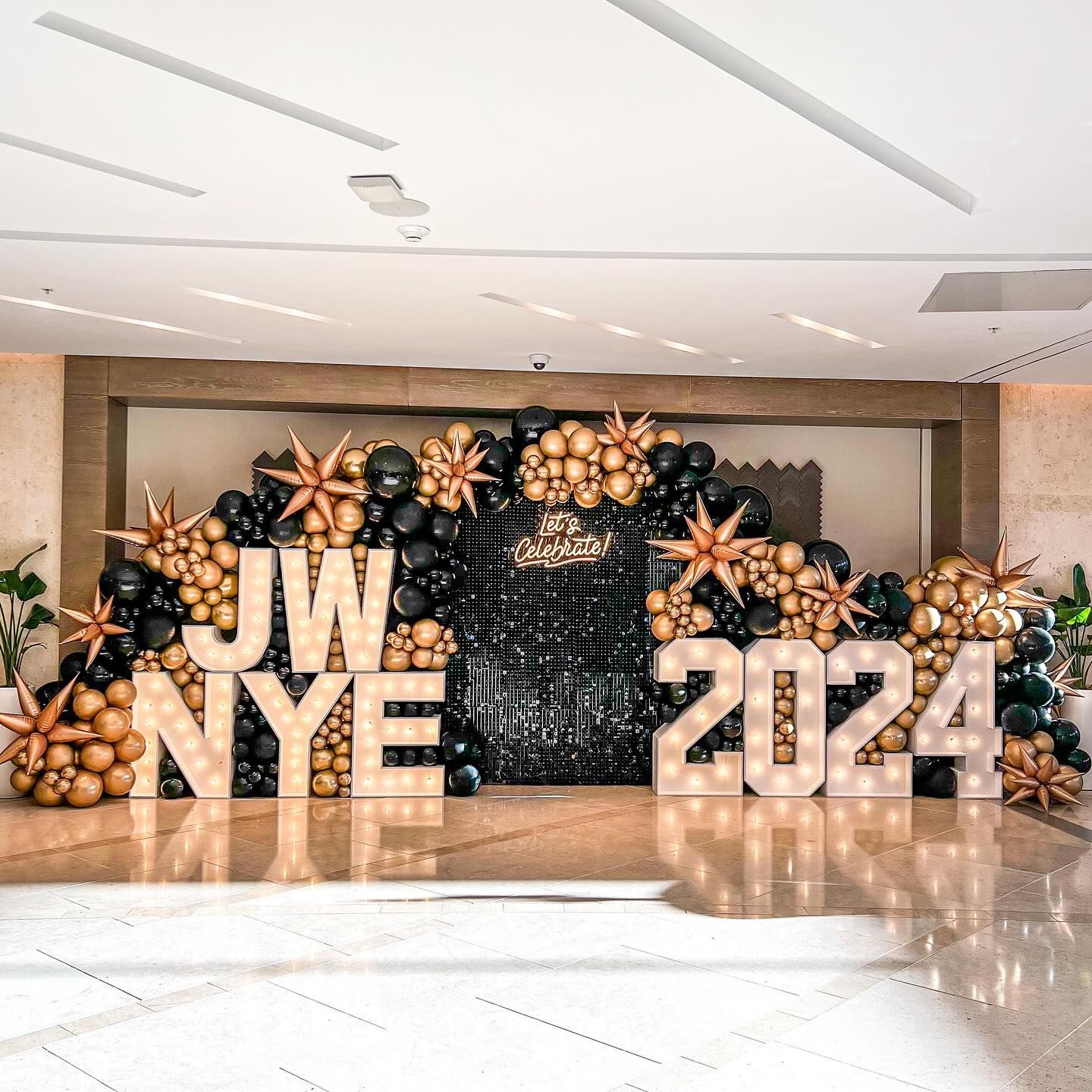 New Year's Eve 2024 display with black and gold balloons, illuminated letters reading