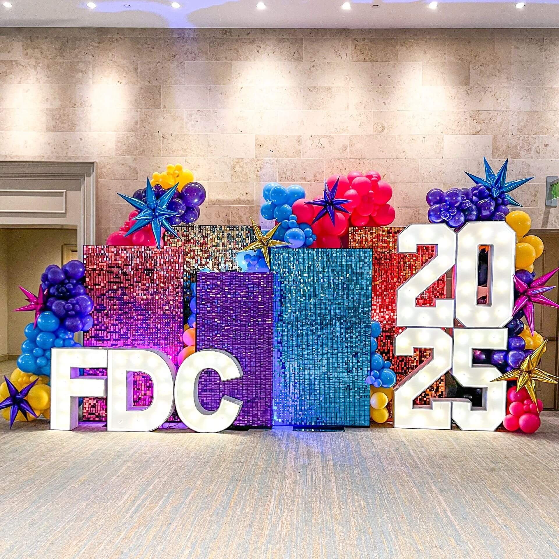 Colorful FDC 2025 display with large white letters and shimmer wall decorations in a lobby