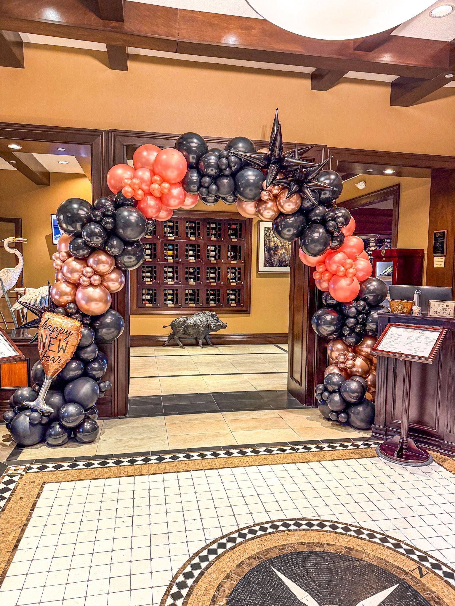 Balloon arch in black and rose gold decorates an entryway with a tile floor.