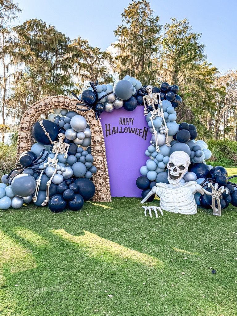Purple Halloween backdrop framed by blue balloons and skeleton decorations on a grassy lawn