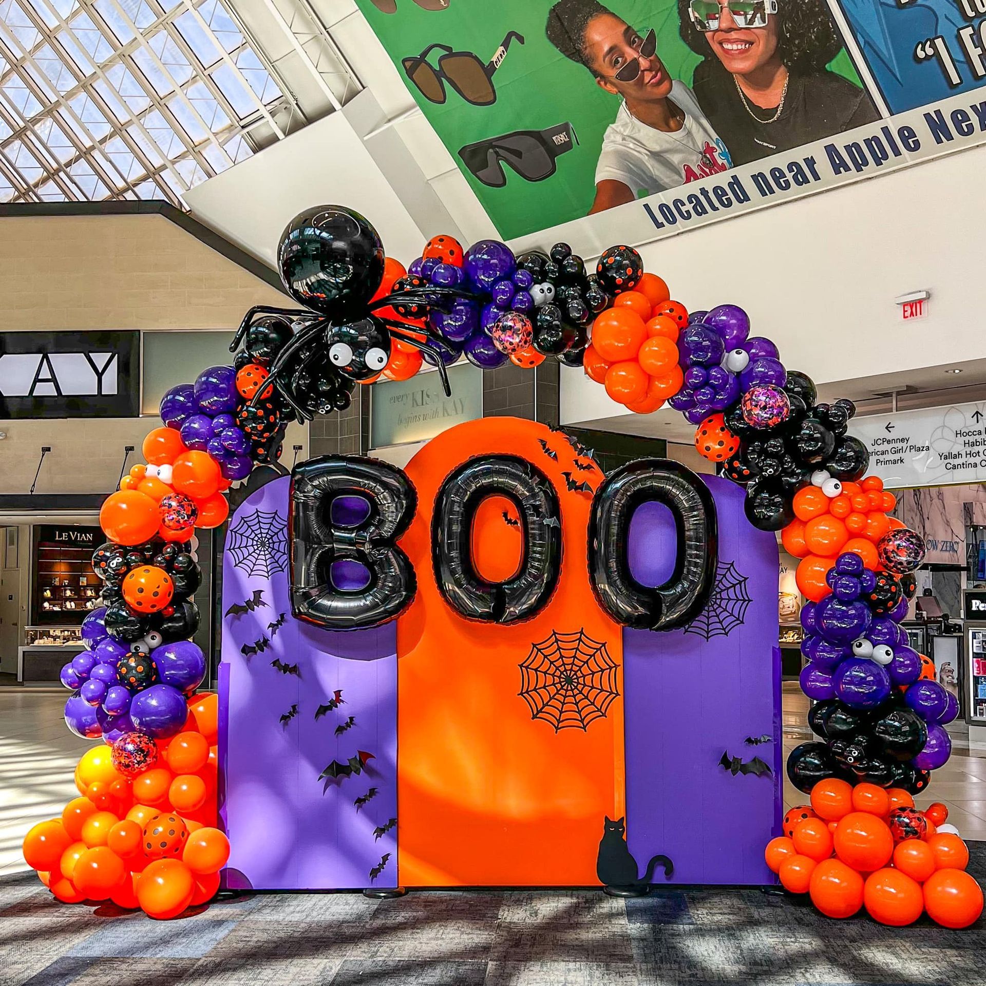 Orange, purple, and black balloon arch with “BOO” letters at a Halloween display in a school lobby.