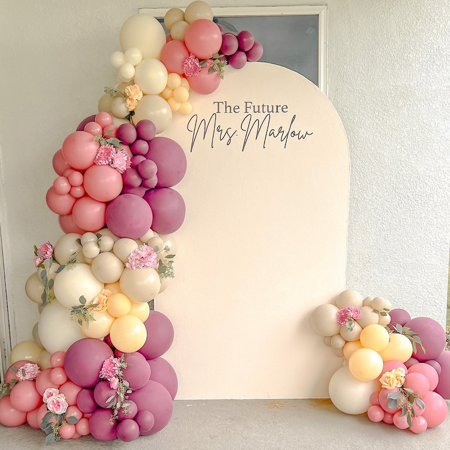 A bunch of pink and purple balloons are hanging from a wall.