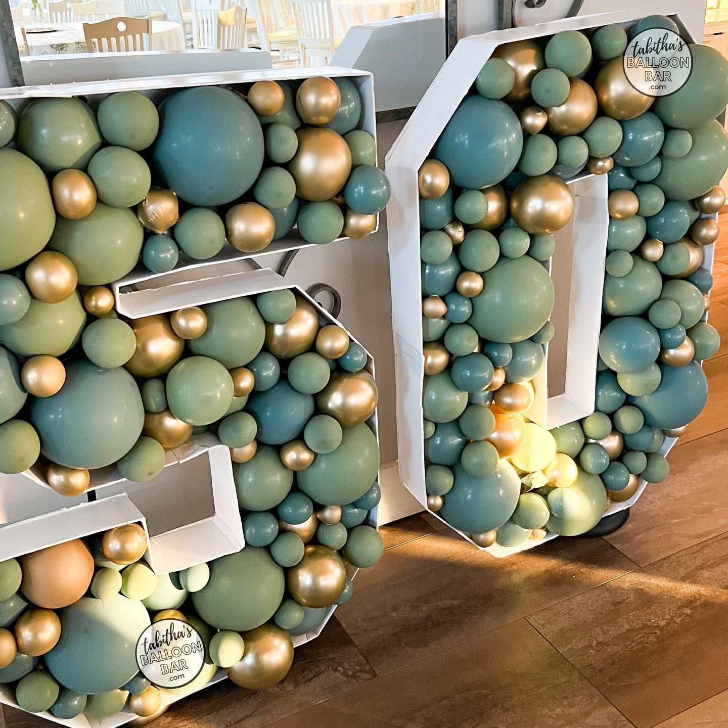 The number 50 is made of balloons and is sitting on a wooden floor.