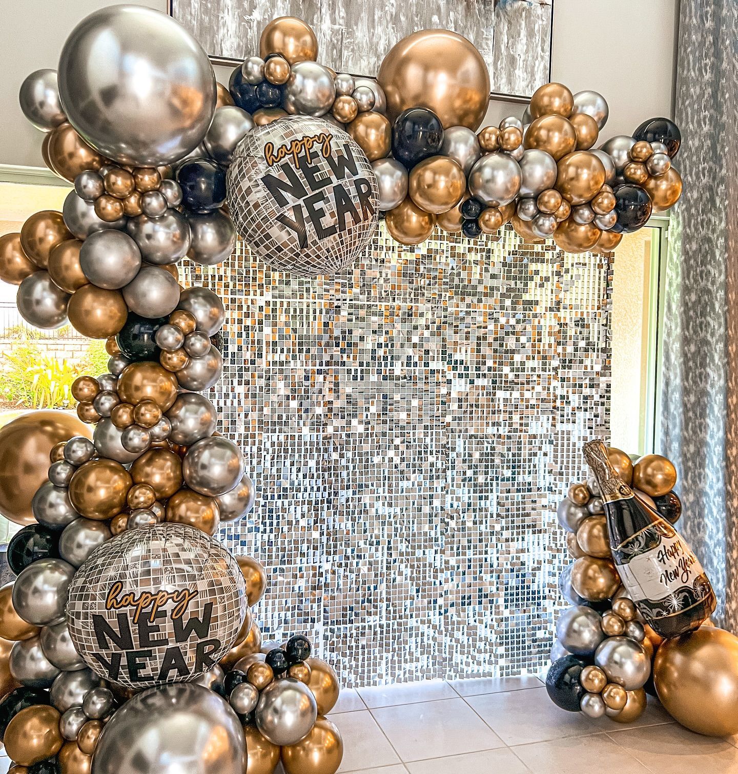 New Year's Eve balloon arch in gold, silver, and black, with a disco ball and champagne bottle.