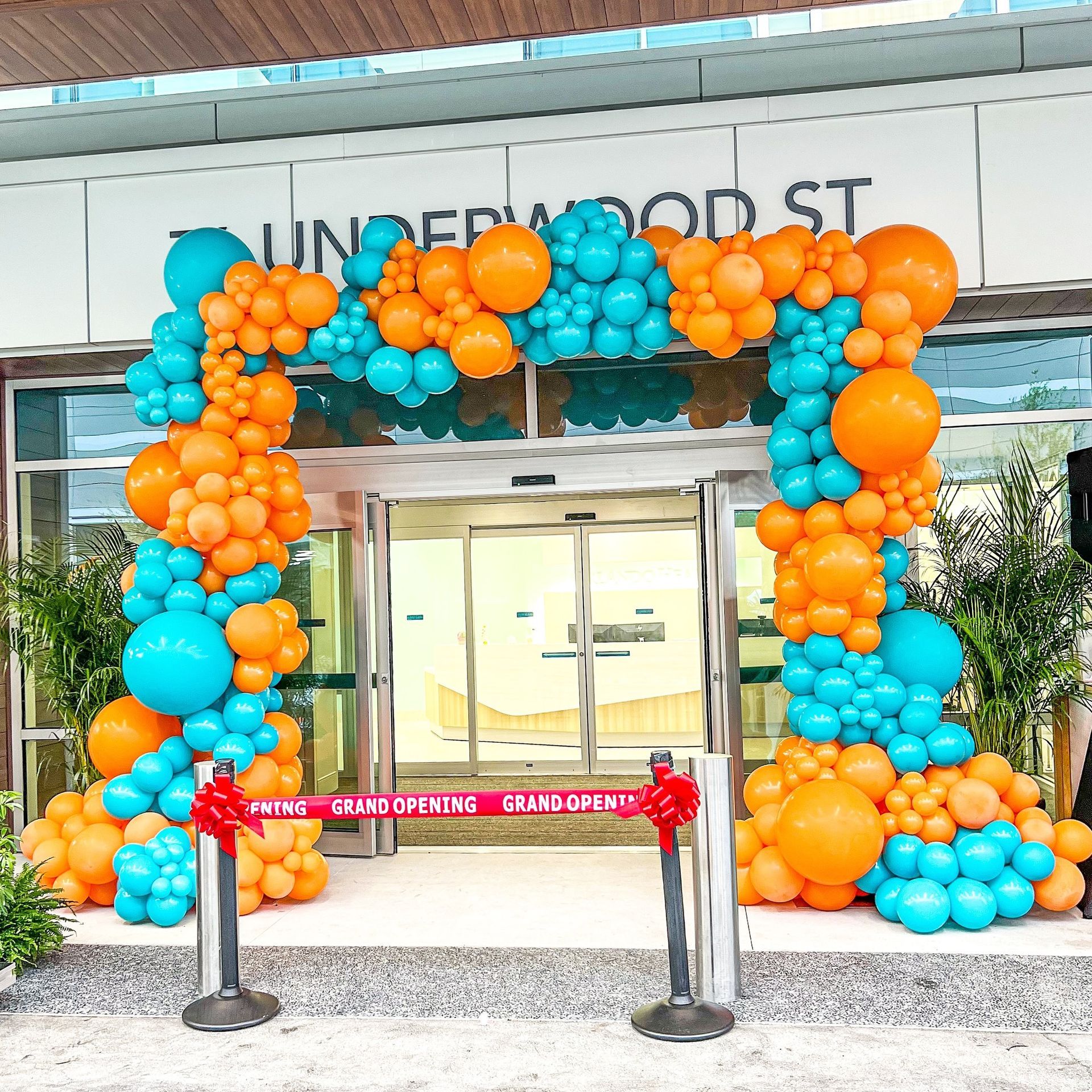 Grand opening at Underwood Street: Arch of blue and orange balloons frames entrance with red ribbon.