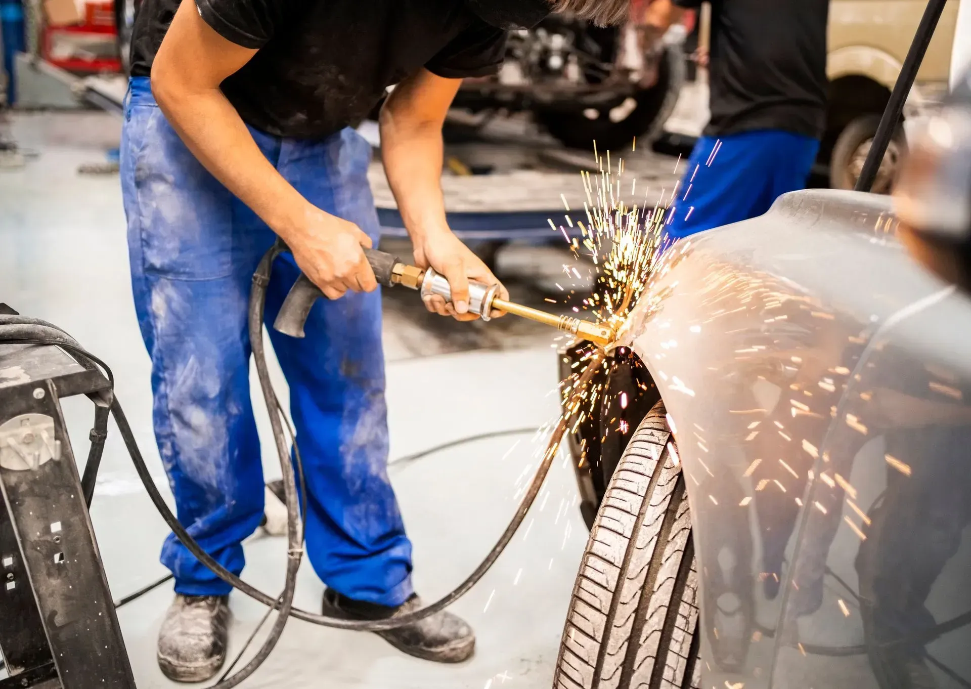 Mechanic using a welding torch on a car, sparks flying in a garage.
