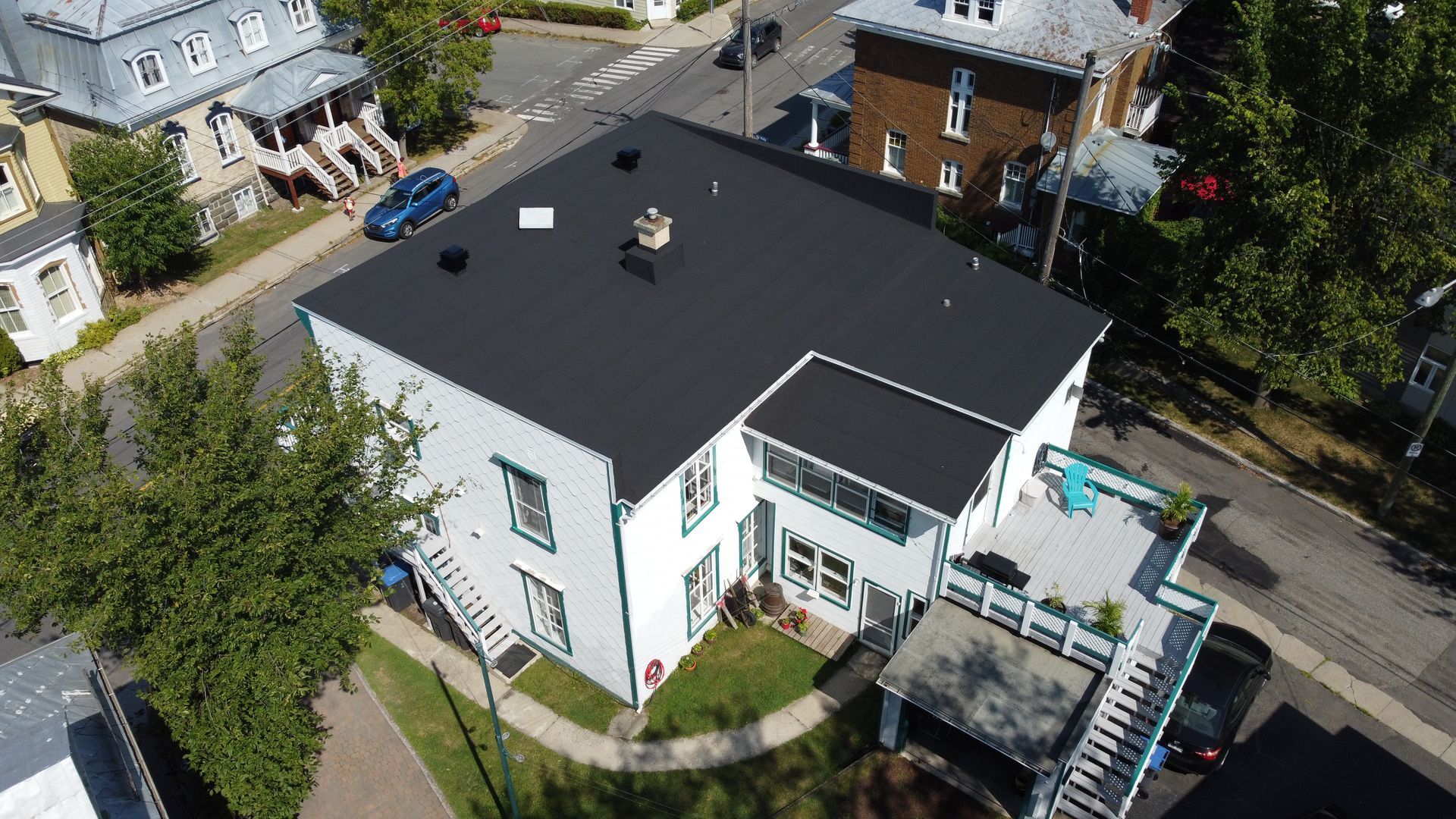 Vue aérienne d'une maison blanche avec un toit noir et un porche d'entrée dans un quartier résidentiel.