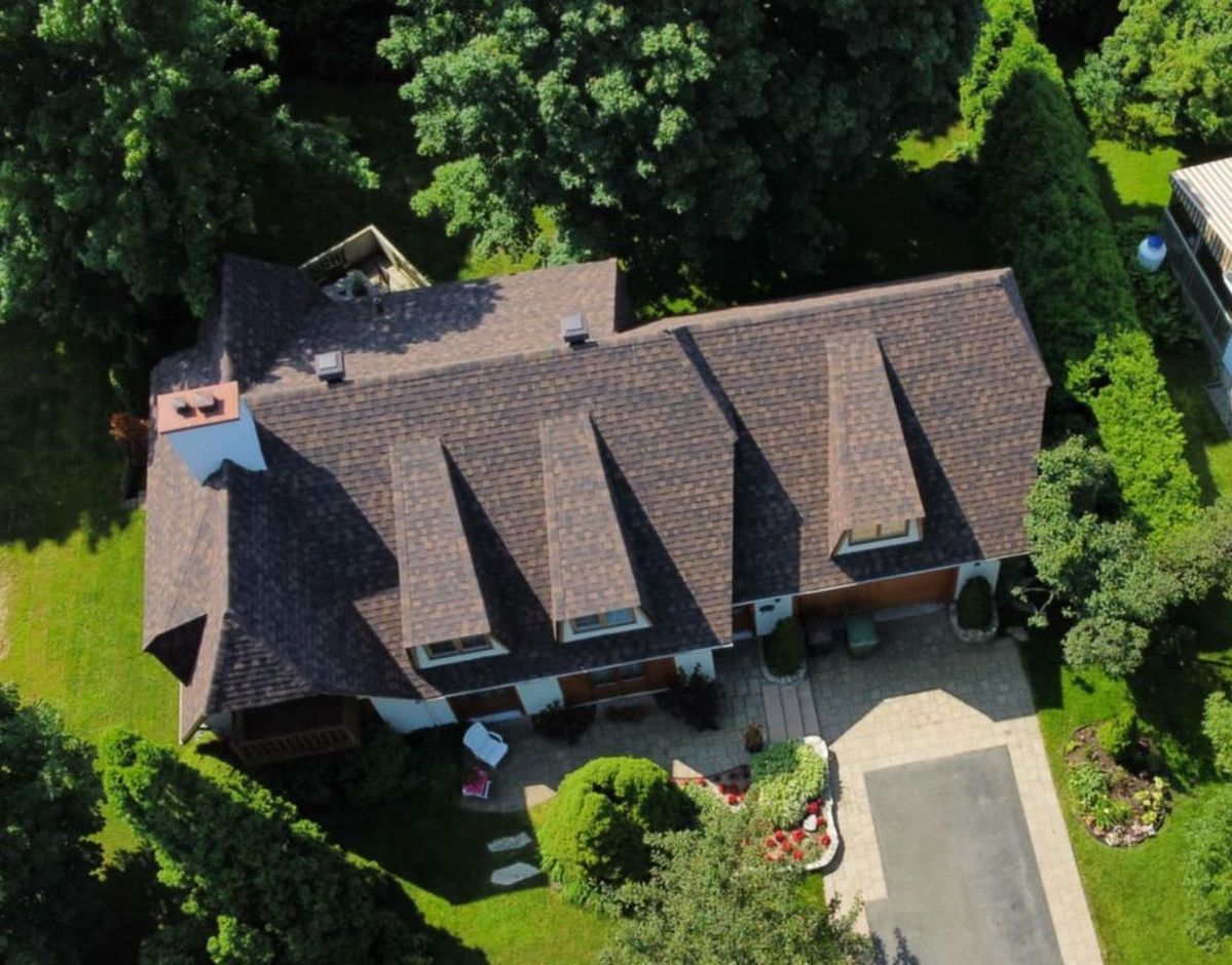 Vue aérienne d'une maison au toit brun, entourée d'arbres verdoyants et d'une allée.