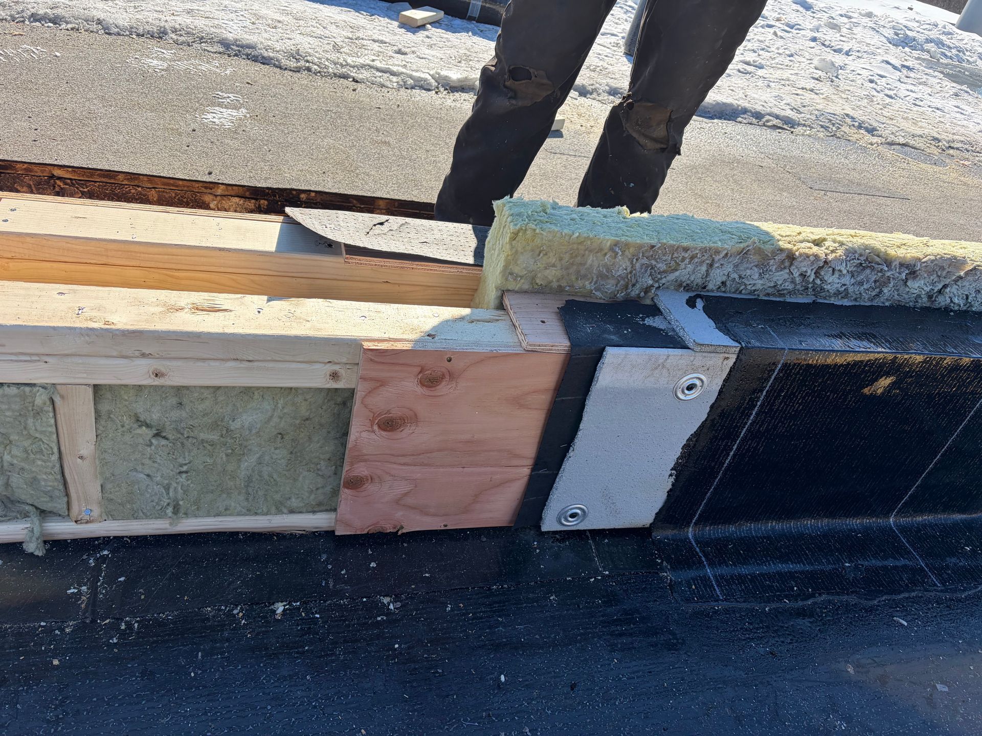 Une personne se tient à côté d'un mur en bois partiellement construit, isolé, avec de la neige en arrière-plan.