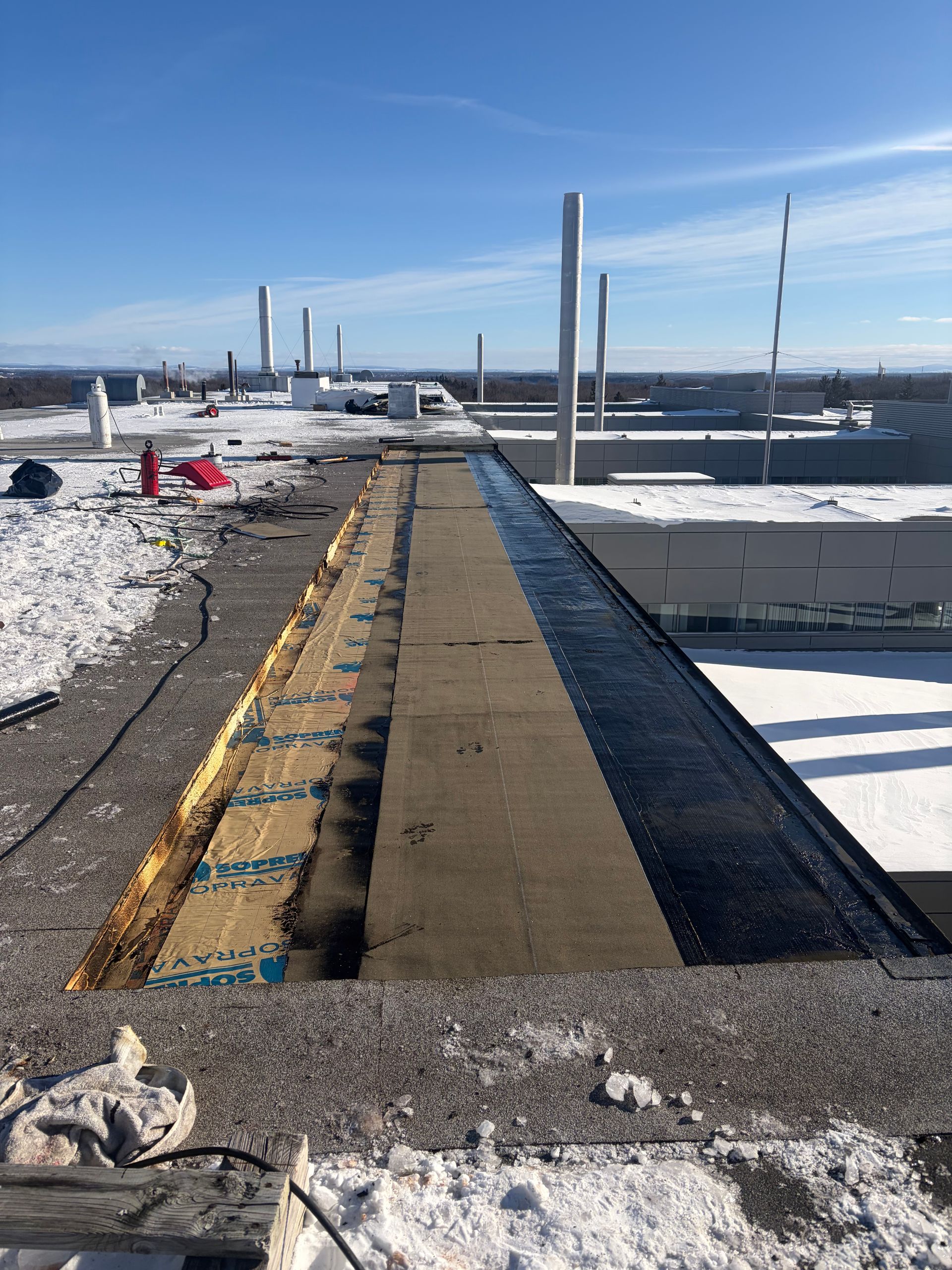 Passerelle enneigée sur le toit, balisée en jaune, avec des cheminées au loin sous un ciel bleu limpide.