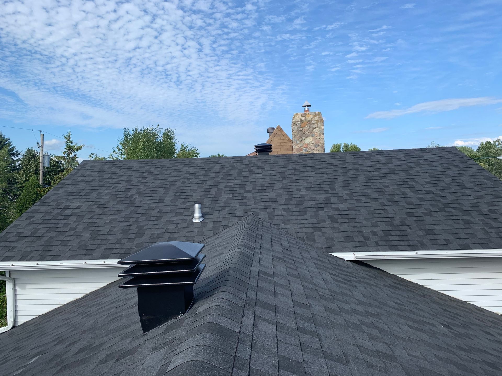 Bardeaux et aérations de toit sur une maison sous un ciel bleu nuageux.