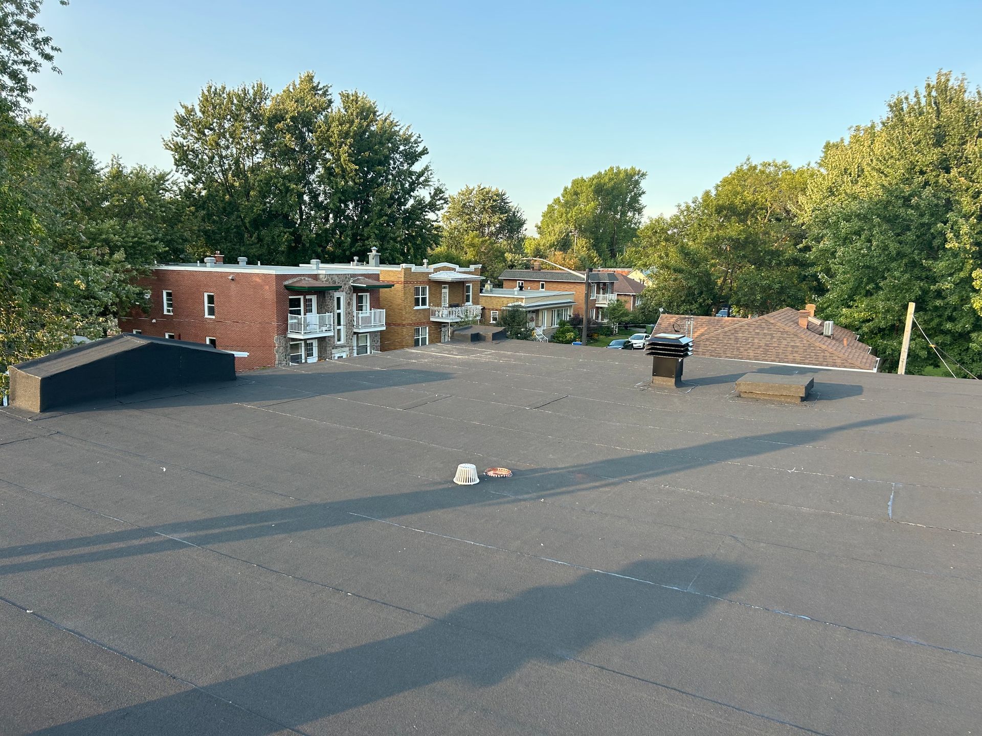 Toit-terrasse recouvert de gravier foncé, avec des aérations et des immeubles d'appartements en briques à proximité, entourés d'arbres.