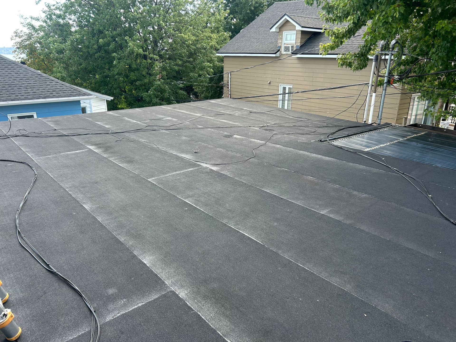 Bardeaux de toit noirs plats avec joints visibles, vus du dessus dans un quartier résidentiel