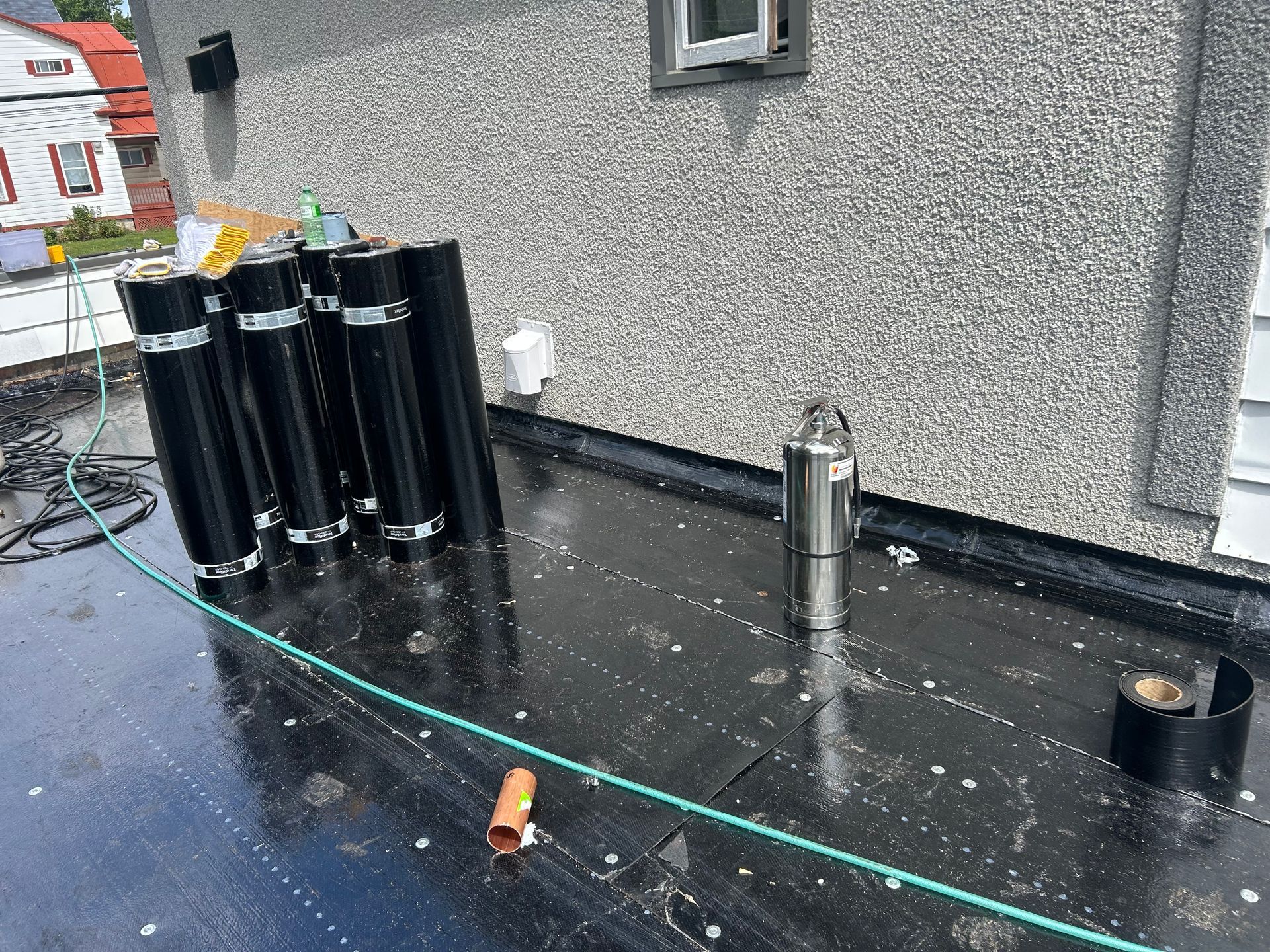 Toiture avec équipements de toiture noirs, un tuyau de ventilation métallique et des outils éparpillés sur une surface humide.