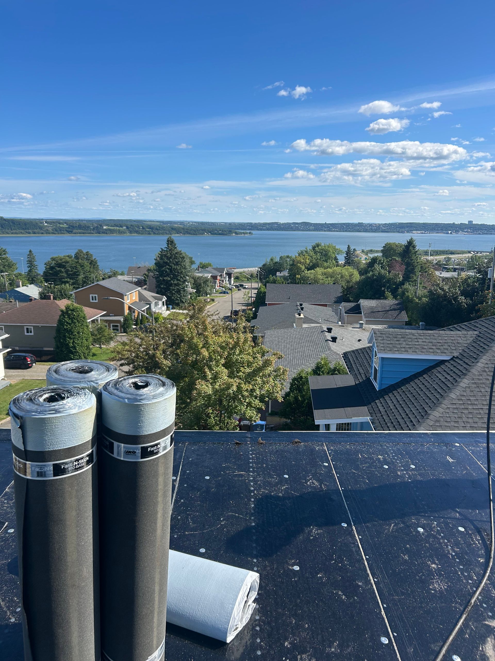 Vue depuis le toit d'un lac et de sa rive lointaine sous un ciel bleu parsemé de nuages, avec des conduits d'aération au premier plan.