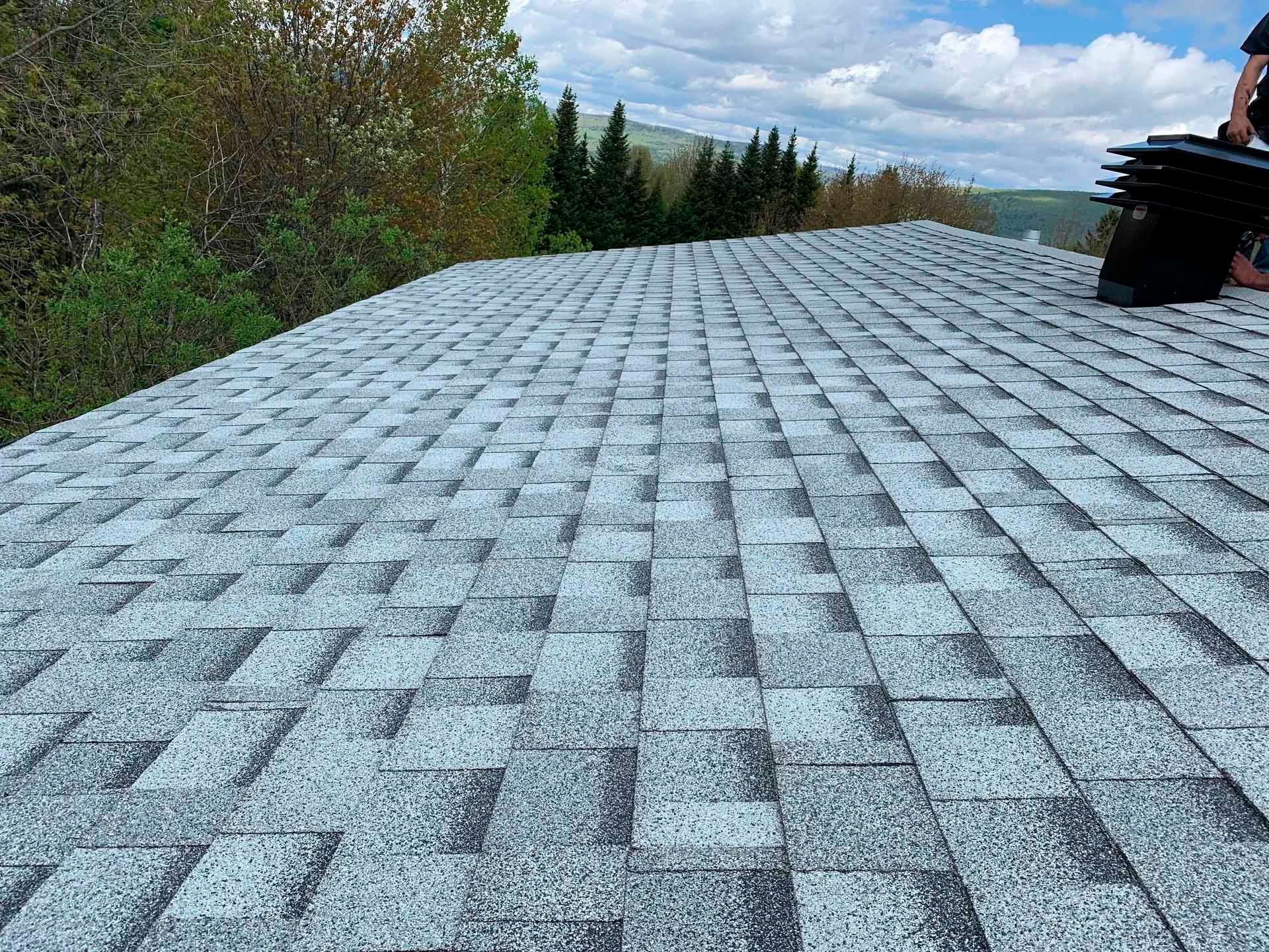 Toit en bardeaux gris vu du ciel, avec des arbres et des collines en arrière-plan.