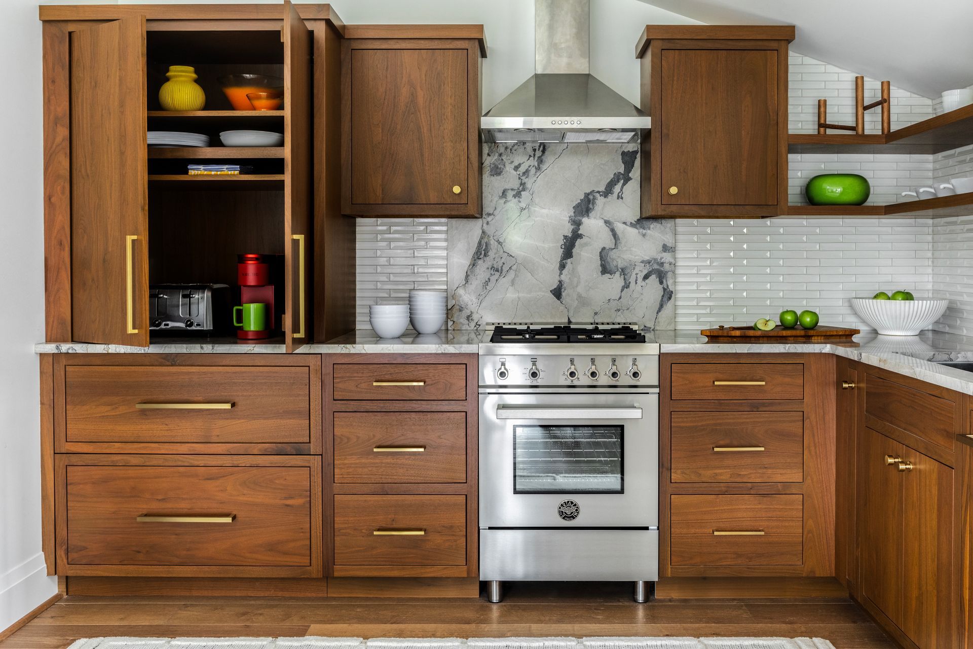 Wooden kitchen cabinets and stainless steel appliances; a built-in pantry with items like a toaster, and a range.