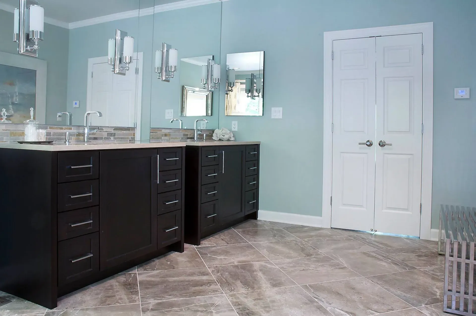 Bathroom with black vanities, light blue walls, white doors, and stone tile flooring.