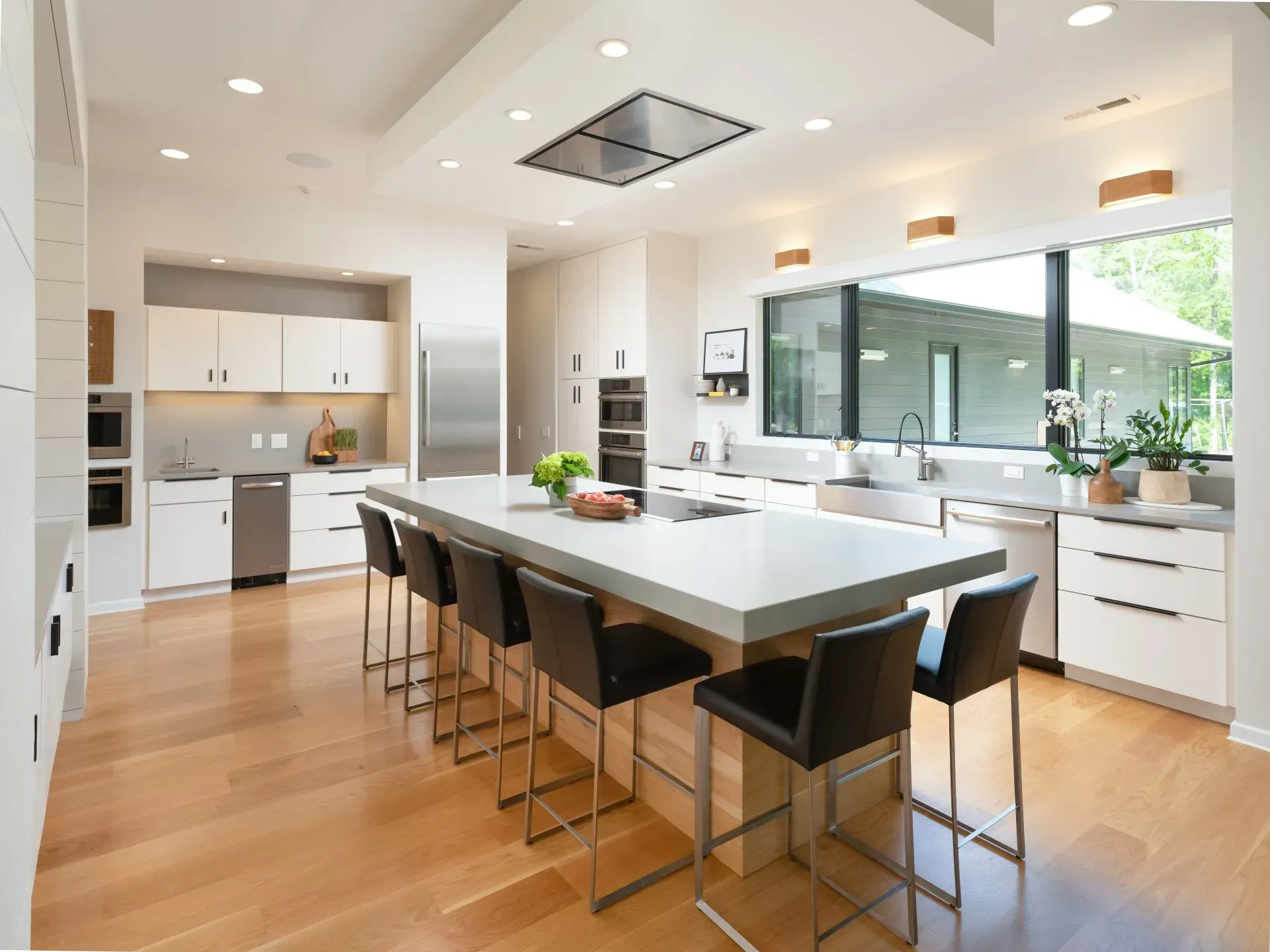 Modern kitchen with large island, stainless steel appliances, light wood floors, and bar stools.