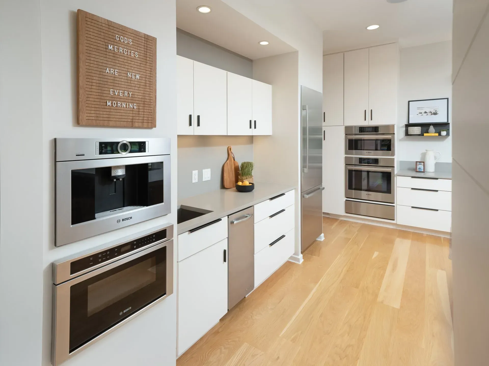 Modern kitchen with light wood floors, stainless steel appliances, and white cabinets.