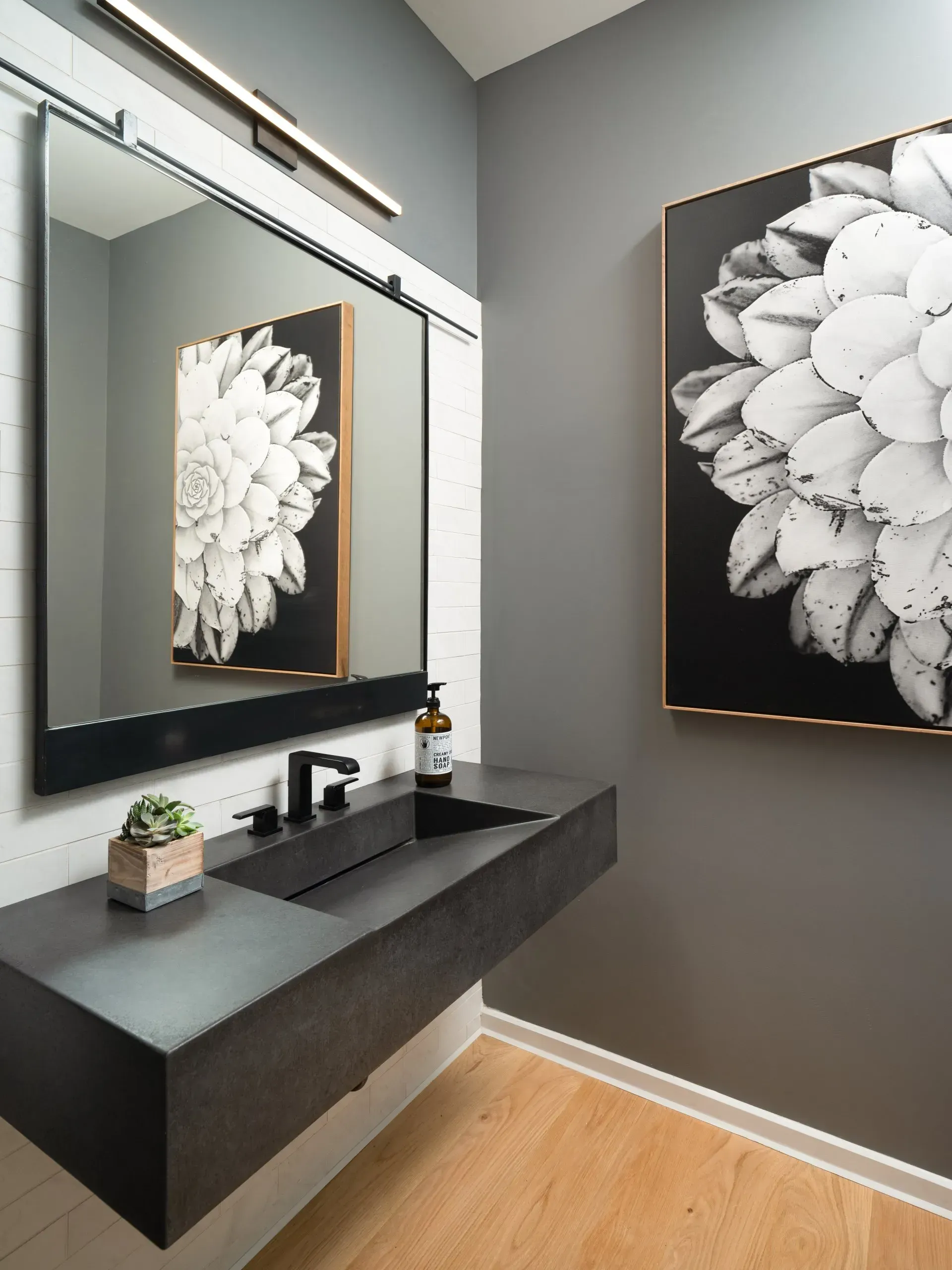 Modern bathroom with gray walls, floating dark sink, large mirror, and floral art.