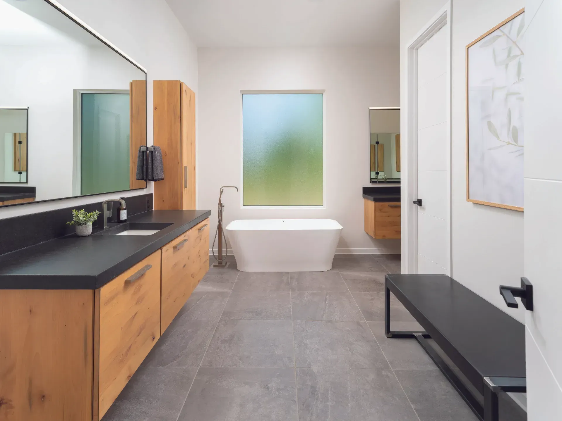 Modern bathroom with a bathtub, black countertops, and wooden cabinets.